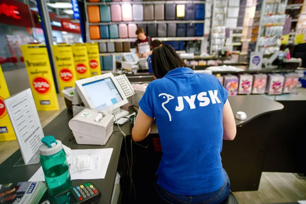 Prodavačka v modrém tričku JYSK obsluhuje pokladnu