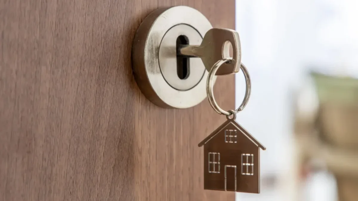 Detail klíče ve dveřích s kovovým přívěskem ve tvaru rodinného domu