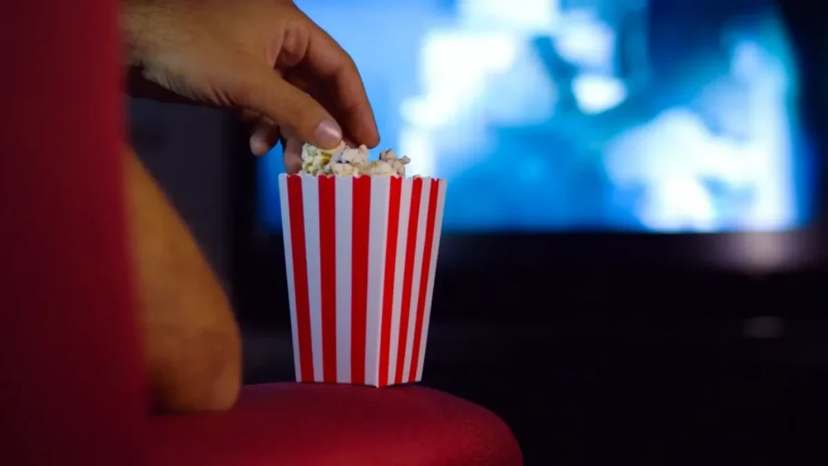 Ruka sahající do krabičky s popcornem před rozmazaným promítaným obrazem filmu
