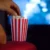 Ruka sahající do krabičky s popcornem před rozmazaným promítaným obrazem filmu