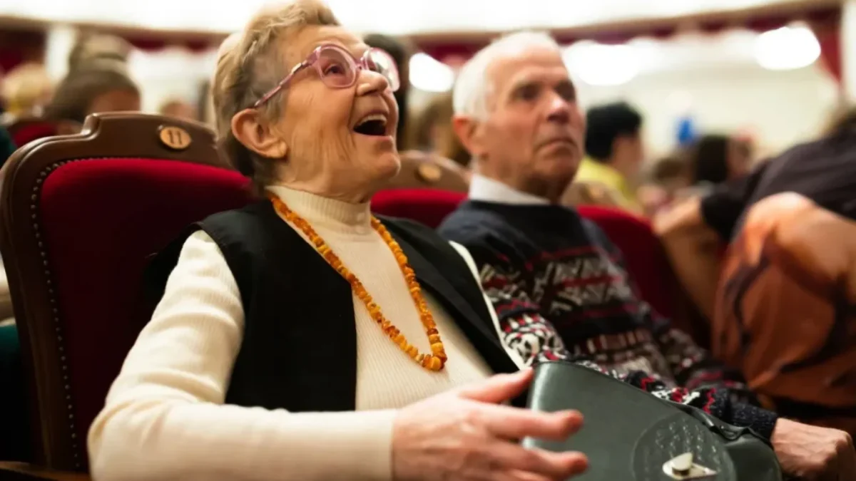 Starší žena se baví při divadelním představení a vedle ní sedí další diváci