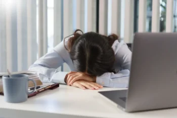 Žena sedící u pracovního stolu s hlavou položenou na rukách