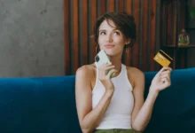 Mladá žena drží mobil, platební kartu a přemýšlí