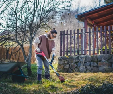 Žena s elektrickým nářadím uklízí spadané listí a trávu na zahradě