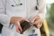 Detail rukou lékaře v plášti, který vytahuje peníze z peněženky