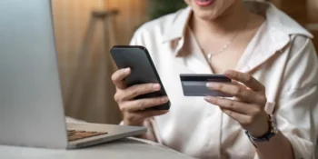 Žena drží v ruce mobilní telefon a platební kartu před otevřeným notebookem