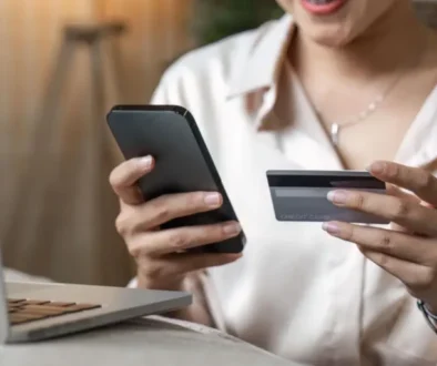 Žena drží v ruce mobilní telefon a platební kartu před otevřeným notebookem