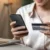 Žena drží v ruce mobilní telefon a platební kartu před otevřeným notebookem