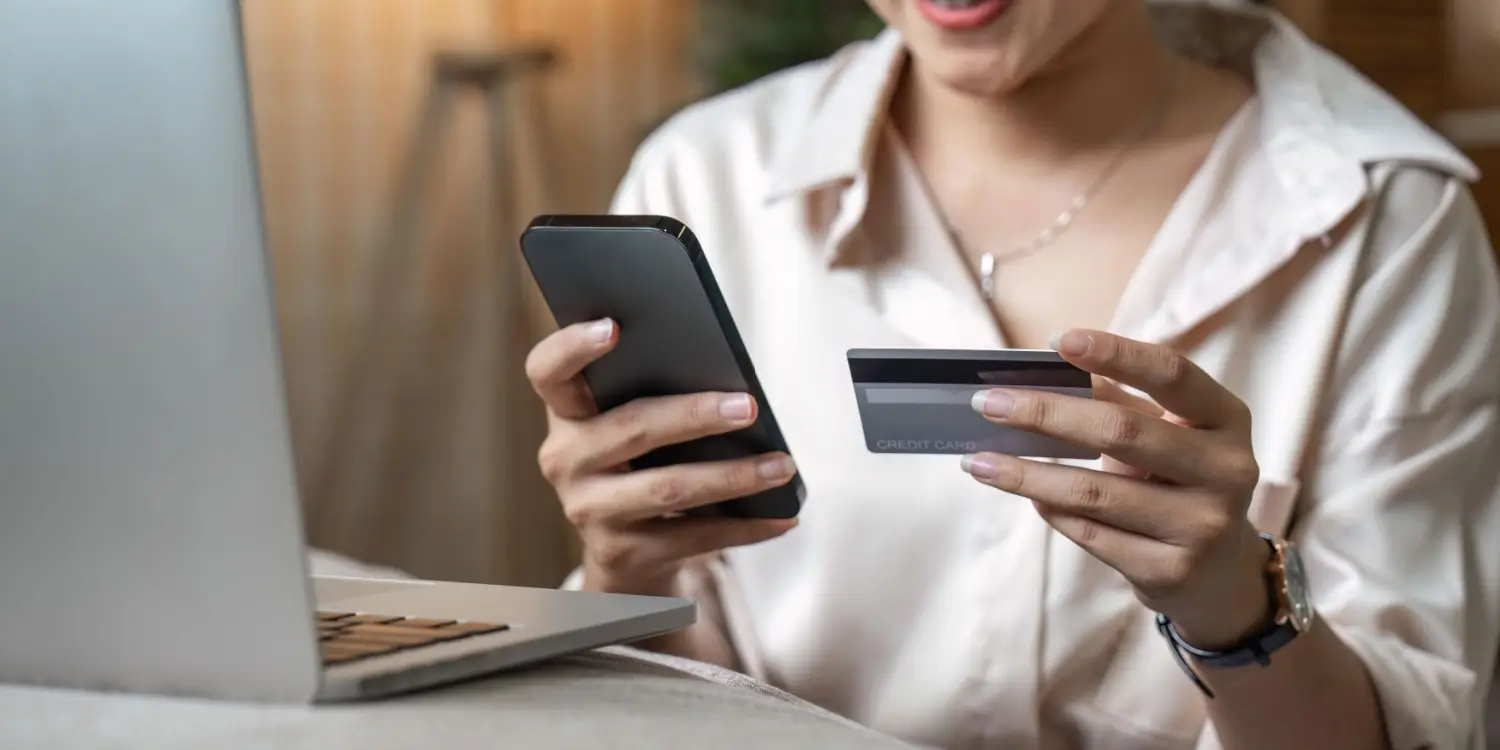 Žena drží v ruce mobilní telefon a platební kartu před otevřeným notebookem