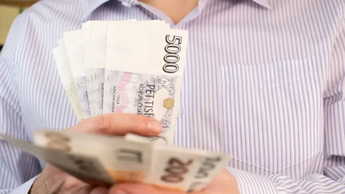 Muž v košili držící několik českých bankovek