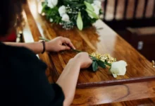 Pozůstalá pokládá bílou růži na dřevěnou rakev při posledním rozloučení