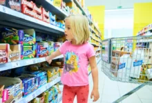 Dívka v růžovém prochází kolem regálu se sladkostmi