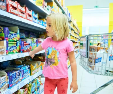 Nejlevnější supermarket s potravinami nemá žádnou reklamu. Dívka v růžovém prochází kolem regálu se sladkostmi