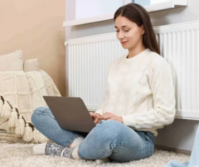 Žena se opírá o topení a pracuje na notebooku