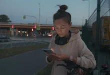 Žena stojí na ulici a kouká do telefonu