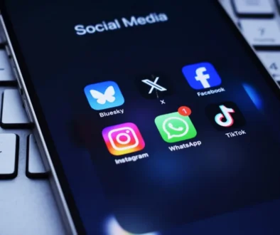 Na obrazovce telefonu je otevřená složka „Social Media“ se šesti ikonami aplikací: Bluesky, X (dříve Twitter), Facebook, Instagram, WhatsApp.