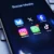 Na obrazovce telefonu je otevřená složka „Social Media“ se šesti ikonami aplikací: Bluesky, X (dříve Twitter), Facebook, Instagram, WhatsApp.