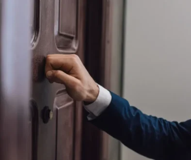 Detail ruky muže v saku klepajícího na dveře