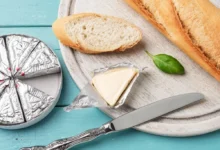 Plátek bagety s rozbaleným trojúhelníčkem taveného sýra na dřevěném prkénku s nožem