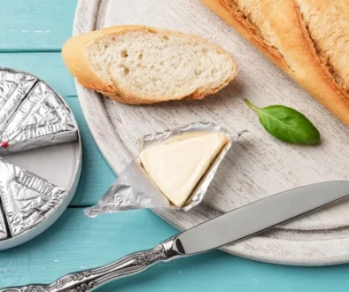 Plátek bagety s rozbaleným trojúhelníčkem taveného sýra na dřevěném prkénku s nožem