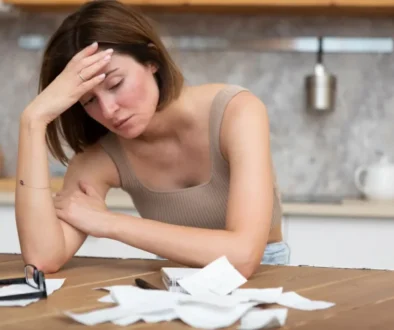 smutná, bezradná žena si drží hlavu v dlaních, na stole před sebou má účtenky