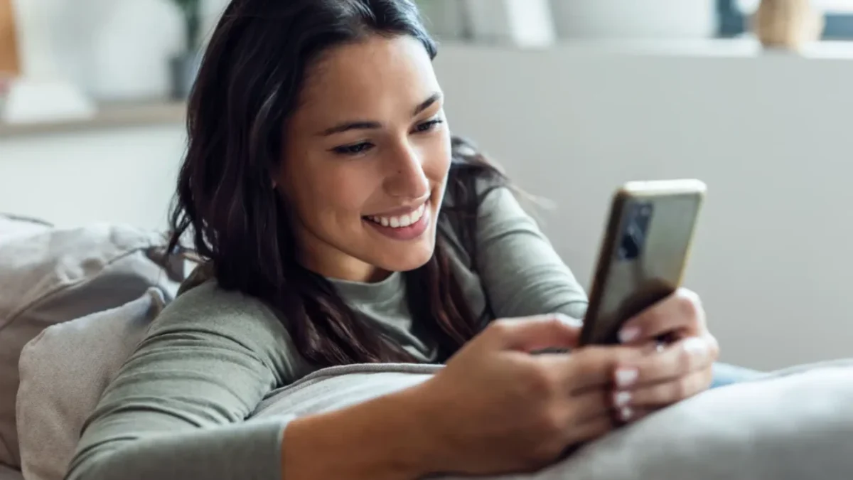 Žena sedí na gauči a drží v ruce mobil