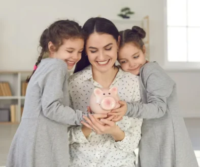 Dvě dcery objímají matku a drží kasičku na peníze