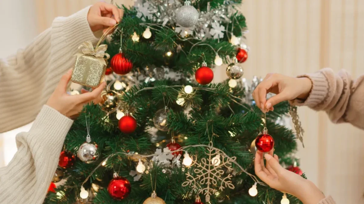 Dva lidé věší ozdoby na vánoční stromek