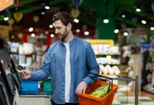 Muž s nákupním košíkem u samoobslužné pokladny
